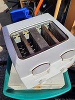 White 4-slot toaster showing top with four bread slots and control levers on the side, placed on a plastic bin.