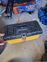 Closed yellow and black plastic toolbox showing the top side with handle and metal latch.
