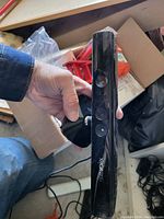 Photo shows one Xbox 360 Kinect sensor held in hand. The device is black with dual cameras and Xbox logo visible, set against a background of boxes and cables.