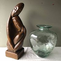 View of plaster statue and glass art vessel together on white surface, showing size and details