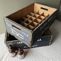 Angle view of two stacked wooden crates with four rows and several columns of bottle partitions and two brown glass beer bottles placed beside them.