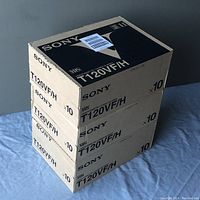 Three sealed Sony VHS tape boxes stacked on top of each other showing taped shipping label on top box.