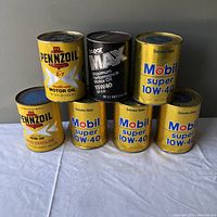 Front view of seven vintage oil cans showing brand and type labels.