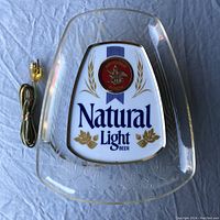 Photo of the sign laying flat with power cord coiled beside it, showing logo, colors, and clear acrylic frame with embossed design.