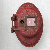Front view of the red oval-shaped ADT fire alarm box with embossed text and glass cover plate showing significant wear and missing screw.