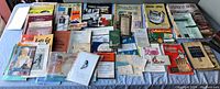 Array of vintage paper ephemera, pamphlets, booklets, and small books laid out on a surface showing various titles and graphics.