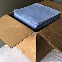 Open cardboard box filled with stacked, blue lint free wipes.