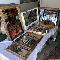 View of multiple beer signs and mirrors shown on tables with visible damage, discoloration and worn frames.