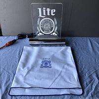 Lite Beer light sign shown upright on blue cloth surface with white cloth storage bag folded in front.