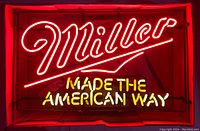 Miller neon beer sign lit in red and yellow in a darkened room.