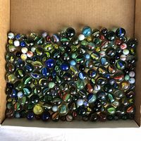 Top down view of a cardboard box filled with approximately 100 multicolored glass marbles of various sizes and swirl designs.