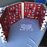 Open display case showing 27 individual 101 Dalmatians plastic figurines in red foam compartments, with Certificate of Authenticity placed inside case on surface.