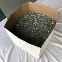 Box filled with numerous clear glass marbles showing quantity and size.