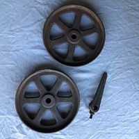 Top view of two 8-inch cast iron wheels and one cast iron handle on a blue cloth background, showing spokes and central holes.