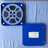 Top view of the blue plastic case with light gray film reel loaded inside, showing the film wound tightly and the white locking pins at corners.