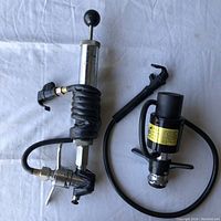 Two beer keg taps on light fabric with hoses, one with taped area and black coiled hose, other with yellow label on metal body.