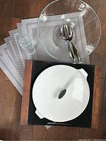 Top view showing wooden buffet server tray with Corningware ceramic dish, glass salad bowl, and stainless steel serving utensils on gray placemats.