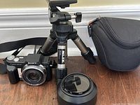 Sony Cyber-shot DSC-H3 camera front with attached lens, Slik Mini tripod, and black camera case on wooden surface.