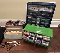 Overall view of sewing and craft lot showing large blue organizer, green thread holder, fabric scissors, pinking shears, and fabric-covered boxes with notions and threads.