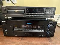 Sony Digital Audio/Video Control Center and Technics Compact Disc Player stacked, both black with digital displays and multiple function buttons, on wooden surface.
