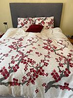 Full bed view showing the duvet cover with red floral branches and the two matching pillow shams, along with a red corduroy decorative pillow in the center.