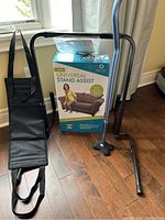 Full lot view showing the stand assist device, cane, and the lift assist strap on a hardwood floor near a window.