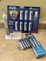 Oral-B electric toothbrush, 9 replacement heads pack, 5-piece Precision Clean heads pack, 4 loose heads with colored rings, and charging base with protective cover.