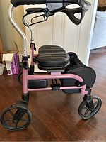 Side view of pink folding walker with padded black seat and hand brakes on ergonomic handles.