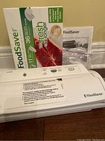 FoodSaver vacuum sealer unit with partially used box of vacuum seal bags and instruction manual behind it.