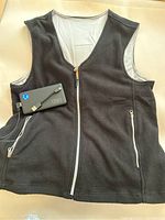 Black fleece heated vest laid flat showing full front with zipper and power bank connected via cable