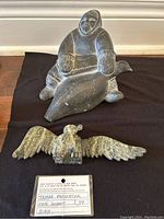 Photo of both Inuit carvings displayed on a black cloth: a hunter with seal and a bird with spread wings, along with a certification card showing the artist Tayara Papigqtok and Cape Dorset provenance.