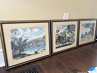 Three framed watercolor paintings depicting island scenes from West Indies, arranged leaning against a wall.