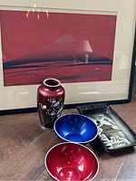 Framed red Mt. Fuji print with red enameled apple blossom vase, red and blue enamel bowls, and vintage Japanese painted ashtray on wooden table.