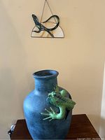 Both the large clay pot with the green lizard sculpted on the side and the small stained glass lizard piece hanging on wall above the pot.