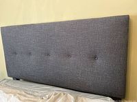Grey padded fabric headboard with button tufting, part of the queen bed frame.