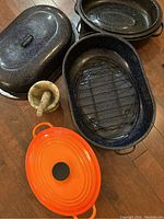Top view of all items in the lot showing large turkey roaster, smaller roaster, Le Creuset Dutch oven, and green marble mortar and pestle.