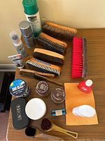 Overall view of shoe shine and leather care items on table including brushes, creams, sprays, cloths, and applicators.
