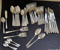 Full view of the complete Oneida Community Tudor Plate silverware set arranged on dark fabric background showing knives, forks, spoons, and serving utensils with floral pattern handles.
