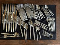 Photo showing all flatware items laid out on black fabric, highlighting knives, forks, spoons, and serving utensils with detailed handles and polished finish.