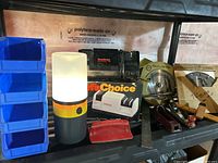 Shelf view with Chef's Choice sharpener, black and orange work light, mini blue stacking bins, and various hand tools including a red measuring tool, metal ruler, planer, and rasp.