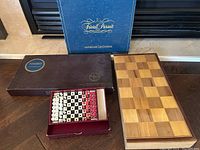 Lot overview showing closed Scrabble box, Trivial Pursuit original edition box, and folding wooden chess/checkers board closed