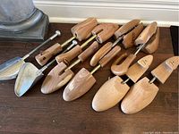 Four sets of wooden men's shoe stretchers and one metal shoe form laid on wooden surface, showing the overall lot content.