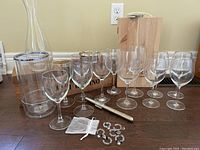 Photo showing two sets of wooden wine boxes and a decanter, wine glasses in sets of two and four, a silver plated coaster, and small metal wine charms and tags.