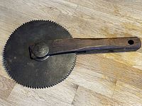 Side view of antique woodworking tool with wooden handle and serrated circular blade showing overall length and blade profile.