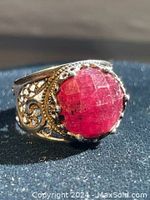 Close-up of ring front showing large faceted burgundy stone and filigree metalwork.