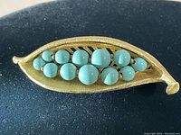 Photo showing the gold-tone leaf brooch with blues stones arranged as peas in a pod