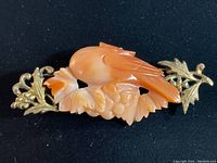 Front view of the pink jade bird brooch with brass floral detailing on black background