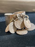 Close-up side view of wide sterling silver ring with multiple stamped small coin charms attached, showing surface texture and attached loops.