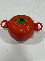 Red kitchen pot shaped like a tomato with green stem lid, shown closed