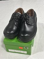 Pair of black leather men's dress shoes on green shoebox, showing front and top view of shoes